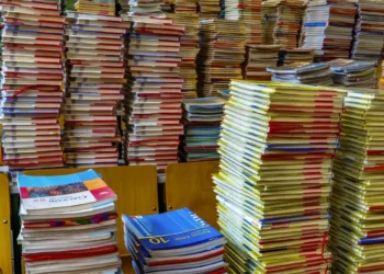 Pile di libri scolastici e quaderni con copertine colorate accatastati su banchi di legno, simili ai testi dei buoni libro