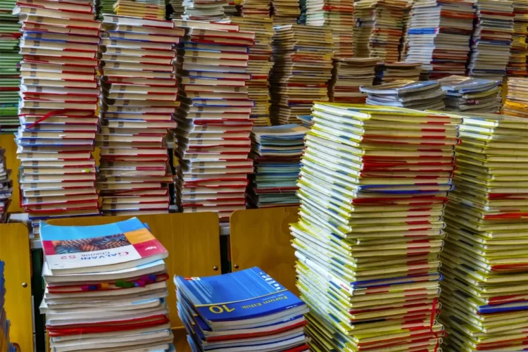 Pile di libri scolastici e quaderni con copertine colorate accatastati su banchi di legno, simili ai testi dei buoni libro