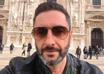 Uomo con barba brizzolata e occhiali da sole, ritratto all'aperto davanti a un edificio monumentale.