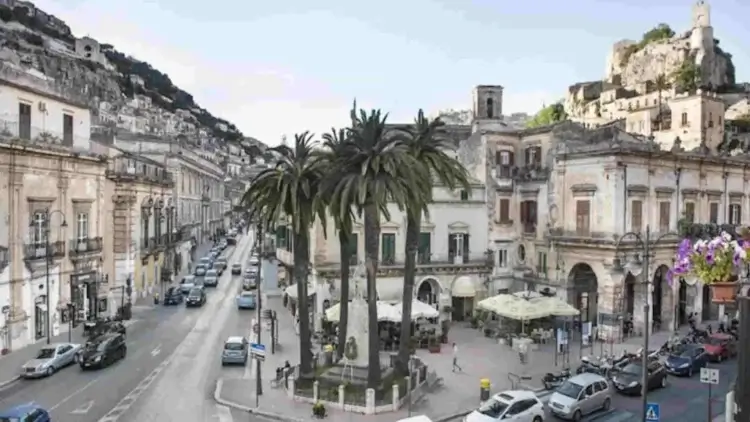Vista di una via del centro storico di Modica con palme, tavolini all'aperto ed edifici storici