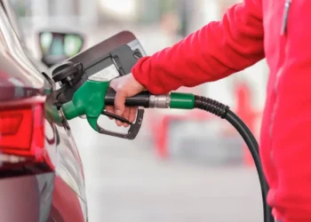 Una mano con la manica di un pile rosso inserisce la pistola verde dell'erogatore nel serbatoio di un'auto per fare carburante