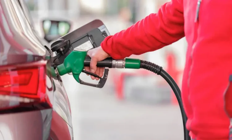 Una mano con la manica di un pile rosso inserisce la pistola verde dell'erogatore nel serbatoio di un'auto per fare carburante