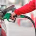 Una mano con la manica di un pile rosso inserisce la pistola verde dell'erogatore nel serbatoio di un'auto per fare carburante