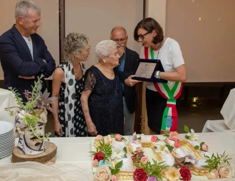 Centenaria di Modica Maria Cavallo riceve una targa dalla sindaca con fascia tricolore, davanti una torta a forma di 100