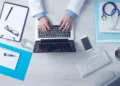 Mani su un laptop, scrivania con stetoscopio e block notes: gestione online di una pratica di malattia