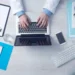 Mani su un laptop, scrivania con stetoscopio e block notes: gestione online di una pratica di malattia