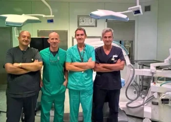 Quattro medici in divisa da sala operatoria a braccia conserte, in una sala di chirurgia vascolare a Vittoria con arco a C