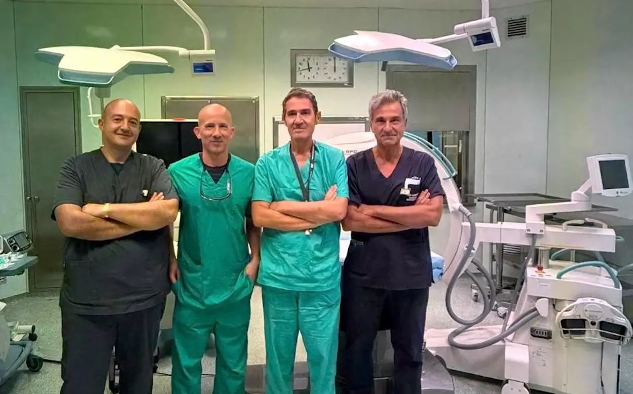 Quattro medici in divisa da sala operatoria a braccia conserte, in una sala di chirurgia vascolare a Vittoria con arco a C