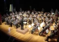 Orchestra Fiati in divisa grigia diretta da un maestro sul palco di un teatro, legata all'intesa tra Conservatorio Bellini e Ispica