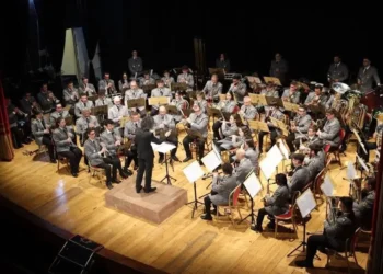 Orchestra Fiati in divisa grigia diretta da un maestro sul palco di un teatro, legata all'intesa tra Conservatorio Bellini e Ispica