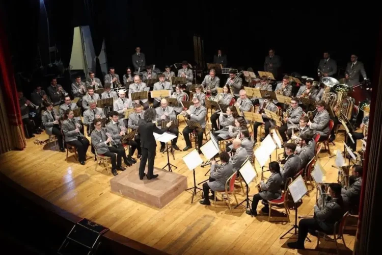 Orchestra Fiati in divisa grigia diretta da un maestro sul palco di un teatro, legata all'intesa tra Conservatorio Bellini e Ispica