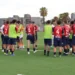 Giocatori del Frigintini in maglia rossoblu riuniti a bordo campo, alcuni con pettorina verde, su erba sintetica