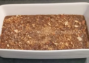 Pirofila bianca con cuddureddi nel mosto scuro, coperti da mandorle tostate tritate e da una spolverata di cannella