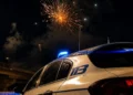 Fuochi d'artificio esplodono nel cielo notturno sopra un'auto della Polizia di Stato con lampeggiante acceso