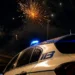 Fuochi d'artificio esplodono nel cielo notturno sopra un'auto della Polizia di Stato con lampeggiante acceso