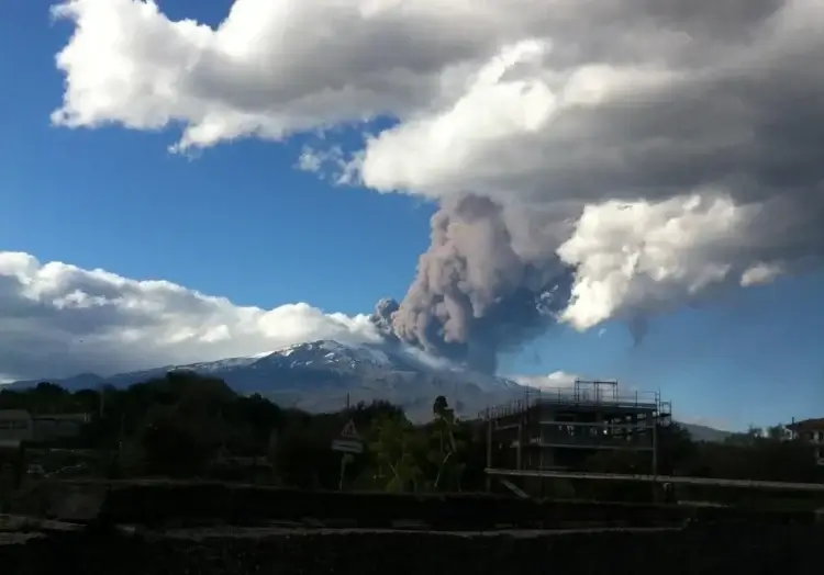 Colonna di cenere e vapore sull'Etna innevato, vista da un abitato alle pendici del vulcano