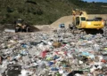Escavatore e bulldozer al lavoro tra cumuli di rifiuti misti in una discarica a cielo aperto