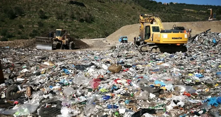 Escavatore e bulldozer al lavoro tra cumuli di rifiuti misti in una discarica a cielo aperto