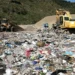 Escavatore e bulldozer al lavoro tra cumuli di rifiuti misti in una discarica a cielo aperto