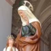 Statua di Sant'Anna accanto a Maria Bambina con corona dorata e mani giunte, sotto un arco decorato