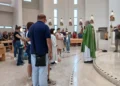 Sacerdote con casula verde davanti a famiglie con bambini piccoli nella chiesa di San Pio X a Ragusa