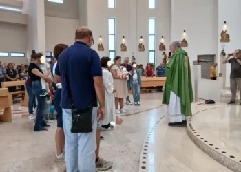 Sacerdote con casula verde davanti a famiglie con bambini piccoli nella chiesa di San Pio X a Ragusa