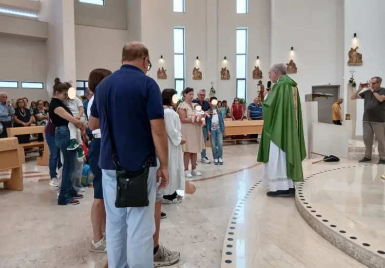 Sacerdote con casula verde davanti a famiglie con bambini piccoli nella chiesa di San Pio X a Ragusa