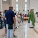 Sacerdote con casula verde davanti a famiglie con bambini piccoli nella chiesa di San Pio X a Ragusa