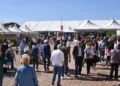 Visitatori tra i padiglioni bianchi della fiera agroalimentare di Ragusa in una giornata di sole, con balle di fieno sullo sfondo
