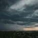 Nuvole temporalesche scure sopra un centro abitato al tramonto, con una cortina di pioggia visibile in lontananza