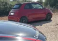 Fiat 500 rossa ferma su uno sterrato, accanto al cofano di un'auto dei Carabinieri