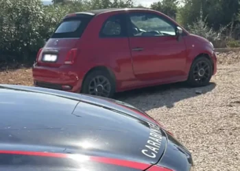 Fiat 500 rossa ferma su uno sterrato, accanto al cofano di un'auto dei Carabinieri
