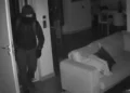 Immagine notturna di sicurezza: un ladro incappucciato entra in casa durante un furto