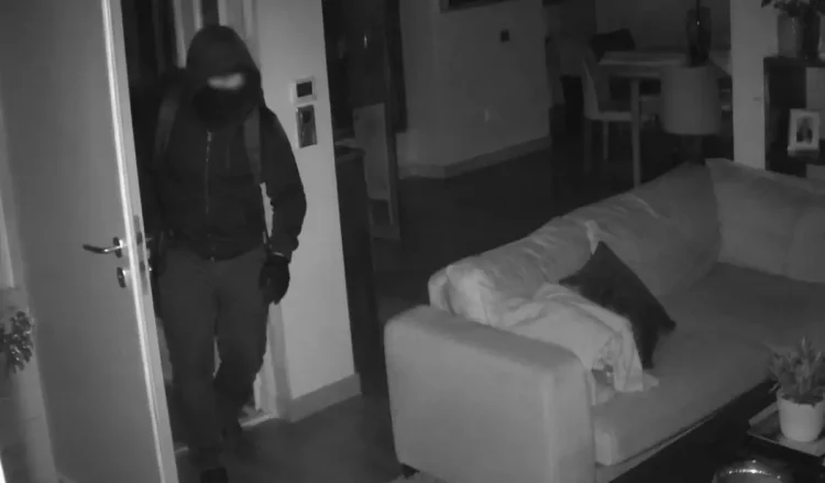 Immagine notturna di sicurezza: un ladro incappucciato entra in casa durante un furto
