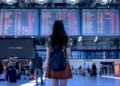 Una giovane donna con zaino osserva il tabellone delle partenze in un aeroporto