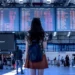 Una giovane donna con zaino osserva il tabellone delle partenze in un aeroporto