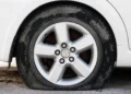 Primo piano di una gomma di un'auto bianca completamente sgonfia e appoggiata a terra su un fondo sterrato
