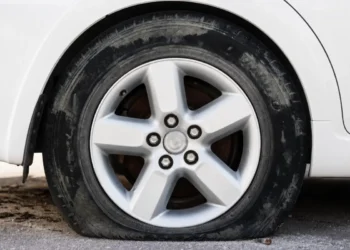 Primo piano di una gomma di un'auto bianca completamente sgonfia e appoggiata a terra su un fondo sterrato
