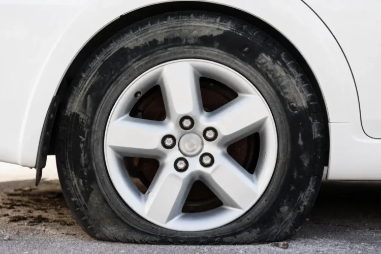 Primo piano di una gomma di un'auto bianca completamente sgonfia e appoggiata a terra su un fondo sterrato