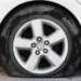 Primo piano di una gomma di un'auto bianca completamente sgonfia e appoggiata a terra su un fondo sterrato
