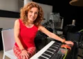 Grazia Colombo sorride al pianoforte, capelli ricci rossi, con un fiore rosso arancio sul leggio dello strumento
