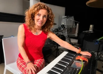 Grazia Colombo sorride al pianoforte, capelli ricci rossi, con un fiore rosso arancio sul leggio dello strumento