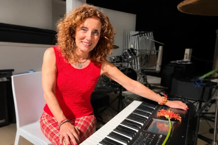 Grazia Colombo sorride al pianoforte, capelli ricci rossi, con un fiore rosso arancio sul leggio dello strumento