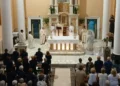 Messa vista dall'alto: celebranti all'altare, fedeli in piedi e, sulla destra, la statua dell'Immacolata