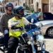 Due persone in sella a una moto con caschi integrali davanti al Castello di Donnafugata, a Ragusa, tra auto d'epoca