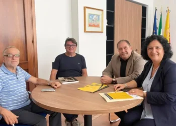 Quattro persone a un tavolo rotondo con opuscoli gialli del progetto In viaggio con i Cabrera, bandiere sullo sfondo