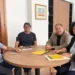 Quattro persone a un tavolo rotondo con opuscoli gialli del progetto In viaggio con i Cabrera, bandiere sullo sfondo