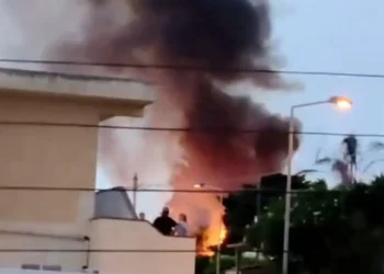 Colonna di fumo nero e fiamme vicino alle case: incendio a Donnalucata, con alcune persone che osservano da un terrazzo