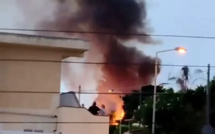 Colonna di fumo nero e fiamme vicino alle case: incendio a Donnalucata, con alcune persone che osservano da un terrazzo