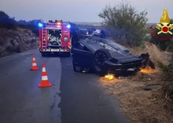 Auto ribaltata su una strada di campagna al crepuscolo, con mezzo dei vigili del fuoco, coni segnaletici e luci blu accese